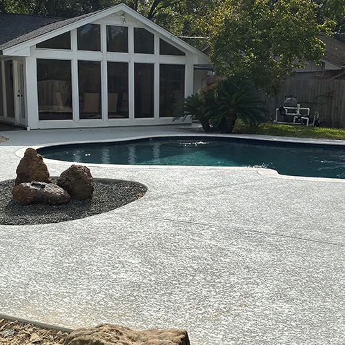 A modern pool with custom concrete deck coating in Houston, designed by Houston Pool Renovations