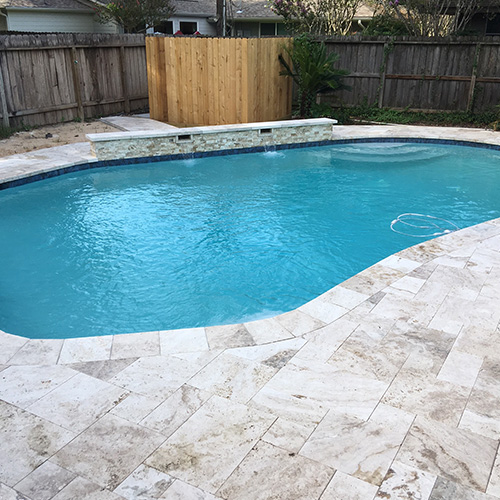 A custom deck featuring natural stone pavers, designed and installed by Houston Pool Renovations, adding elegance to a backyard space.