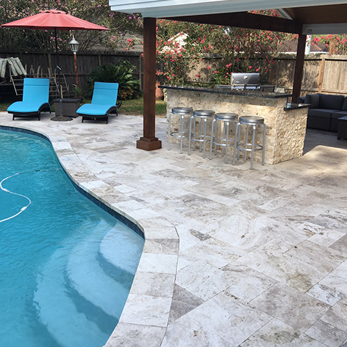 A custom deck featuring natural stone pavers, designed and installed by Houston Pool Renovations, adding elegance to a backyard space.