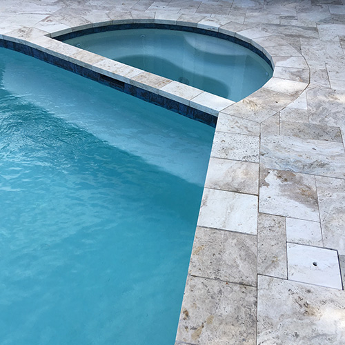 A custom deck featuring natural stone pavers, designed and installed by Houston Pool Renovations, adding elegance to a backyard space.