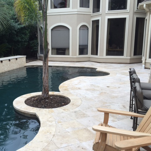 A custom deck featuring natural stone pavers, designed and installed by Houston Pool Renovations, adding elegance to a backyard space.