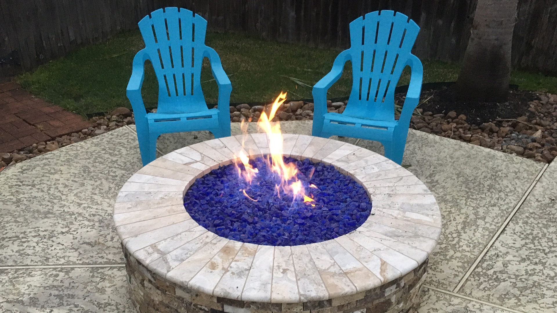 A custom-built stone fire pit near a pool in Houston, surrounded by elegant outdoor seating, designed by Houston Pool Renovations.