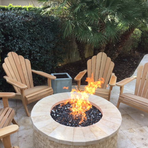 A custom-built stone fire pit near a pool in Houston, surrounded by elegant outdoor seating, designed by Houston Pool Renovations.