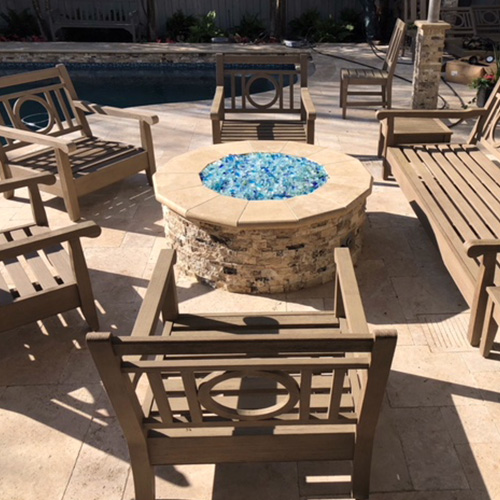 A custom-built stone fire pit near a pool in Houston, surrounded by elegant outdoor seating, designed by Houston Pool Renovations.