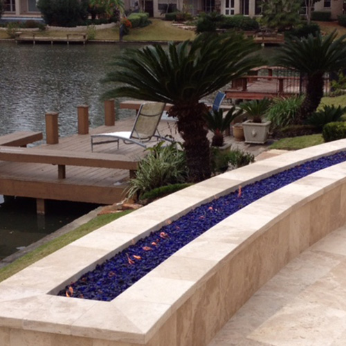 A custom-built stone fire pit near a pool in Houston, surrounded by elegant outdoor seating, designed by Houston Pool Renovations.