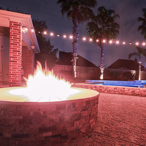 A custom-built stone fire pit near a pool in Houston, surrounded by elegant outdoor seating, designed by Houston Pool Renovations.