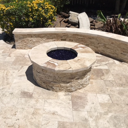 A custom-built stone fire pit near a pool in Houston, surrounded by elegant outdoor seating, designed by Houston Pool Renovations.